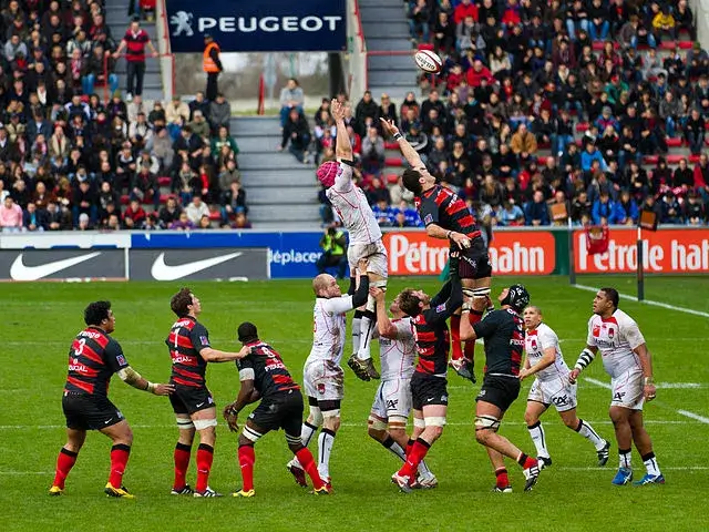 Two rugby teams form a lineout, each lifting a player into the air as the ball in thrown in